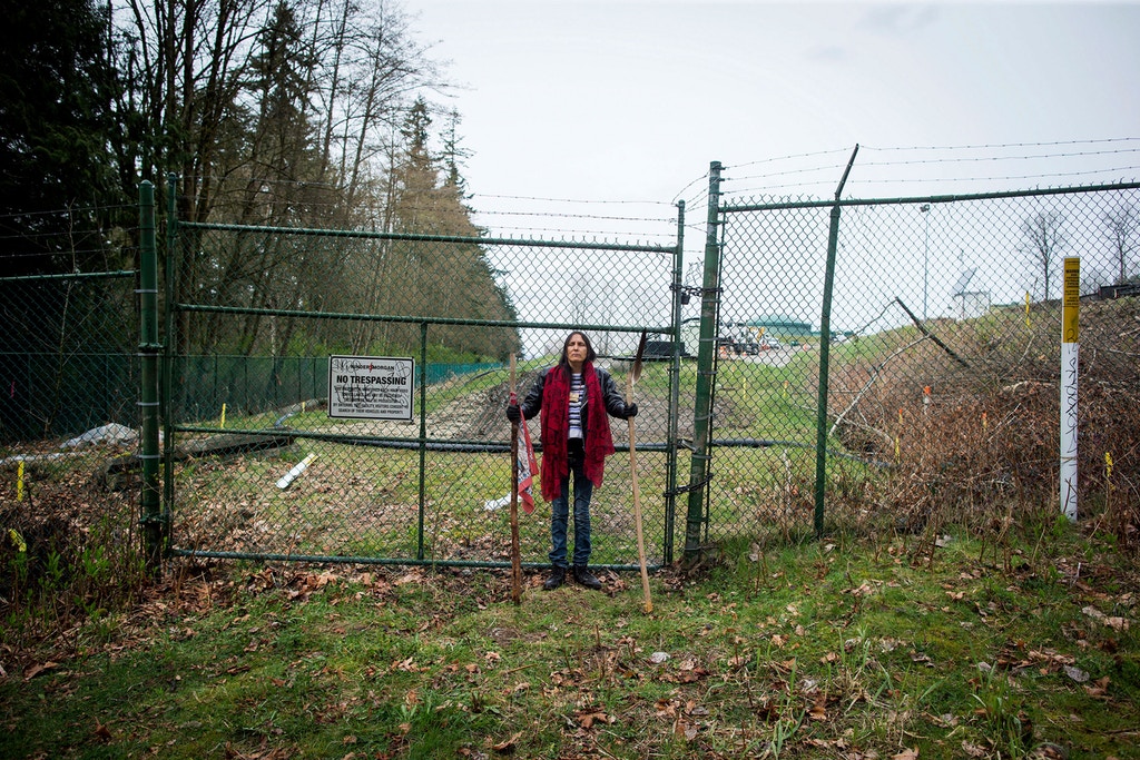 Kat Roivas, who is opposed to the expansion of the Kinder Morgan Trans Mountain pipeline, stands at an access gate at the company's property near an area where work is taking place, in Burnaby, B.C., on Monday April 9, 2018. The Houston, Texas, based company announced Sunday it has suspended all non-essential activities and related spending on the pipeline expansion that would carry Alberta bitumen to an export terminal near Vancouver. (Darryl Dyck/The Canadian Press via AP)