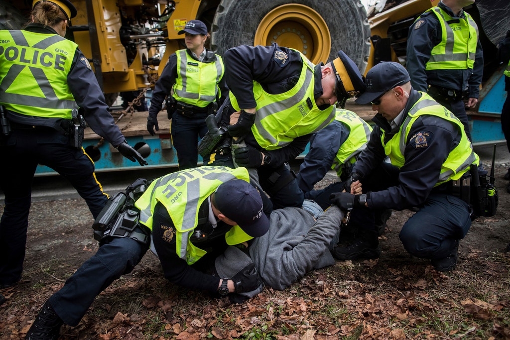 Dan Wallace, of the Kwakwaka'wakw First Nation on Quadra Island, is tackled and handcuffed by RCMP officers after attempting to talk to a young man that locked himself to a piece of heavy equipment being delivered to Kinder Morgan in Burnaby, B.C., on Monday March 19, 2018. Wallace was released a short time later without being charged. Numerous protesters who blockaded an entrance - defying a court order - were arrested earlier in the day while protesting the Kinder Morgan Trans Mountain pipeline expansion. (Darryl Dyck/The Canadian Press via AP)