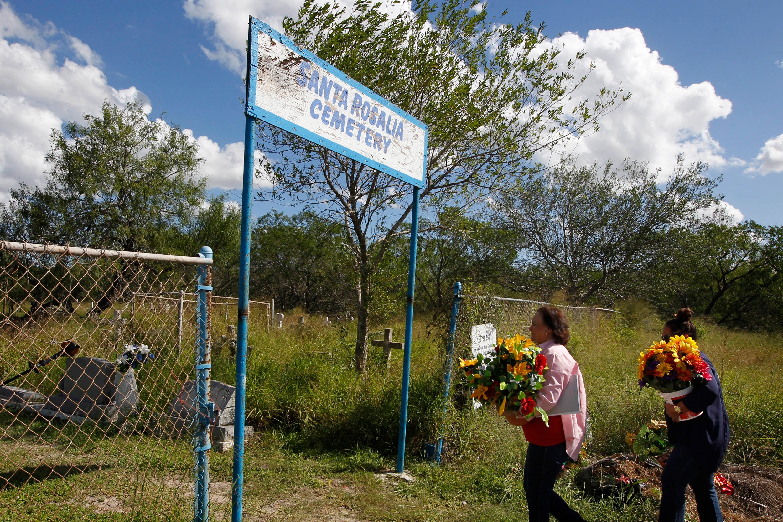 Estela Aguilar Hernandez, left, and her daughter Cecilia Hernandez carry flowers for the graves of deceased relatives into the Santa Rosalia Cemetery on Tuesday, Oct. 24, 2017, in Brownsville, Texas. Hernandez' grandparents and many other relatives are buried at the cemetery, which is located south of the border wall just north of the Rio Grande. Hernandez fears last year's approval of border gate funding will limit access to the cemetery.  (Nathan Lambrecht/The Monitor via AP)