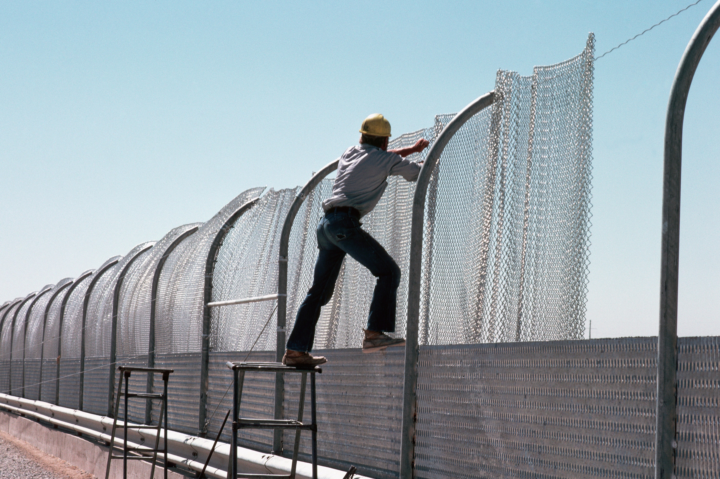 A construction worker pulls steel mesh into place on a section of the galvanized steel fence being built along the border between the United States and Mexico in 1979. The fence, intended to keep illegal aliens from crossing into the US, is known as the "Tortilla Curtain." (Photo by © Stephanie Maze/CORBIS/Corbis via Getty Images)